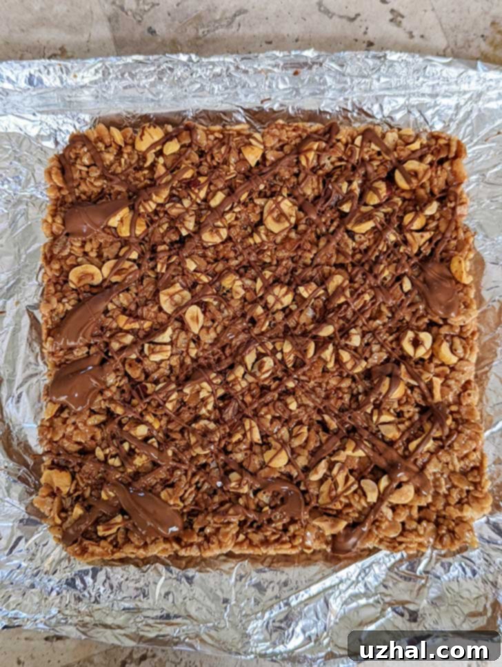 An 8-inch square pan filled with cooling Chocolate Hazelnut Rice Krispies Treats, topped with an optional chocolate drizzle.