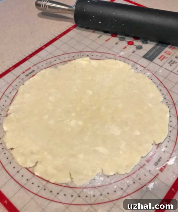Close-up of gluten-free pastry dough being rolled out on a pastry mat, showing the pliable texture and some visible butter chunks.