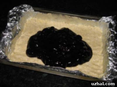 A delicious layer of bright red cherry pie filling spread over a golden-brown crust in a baking pan, ready for the crumb topping.