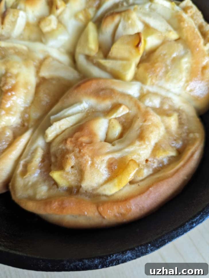 Small batch of Apple Pie Cinnamon Rolls in a cast iron skillet, golden brown and glistening.
