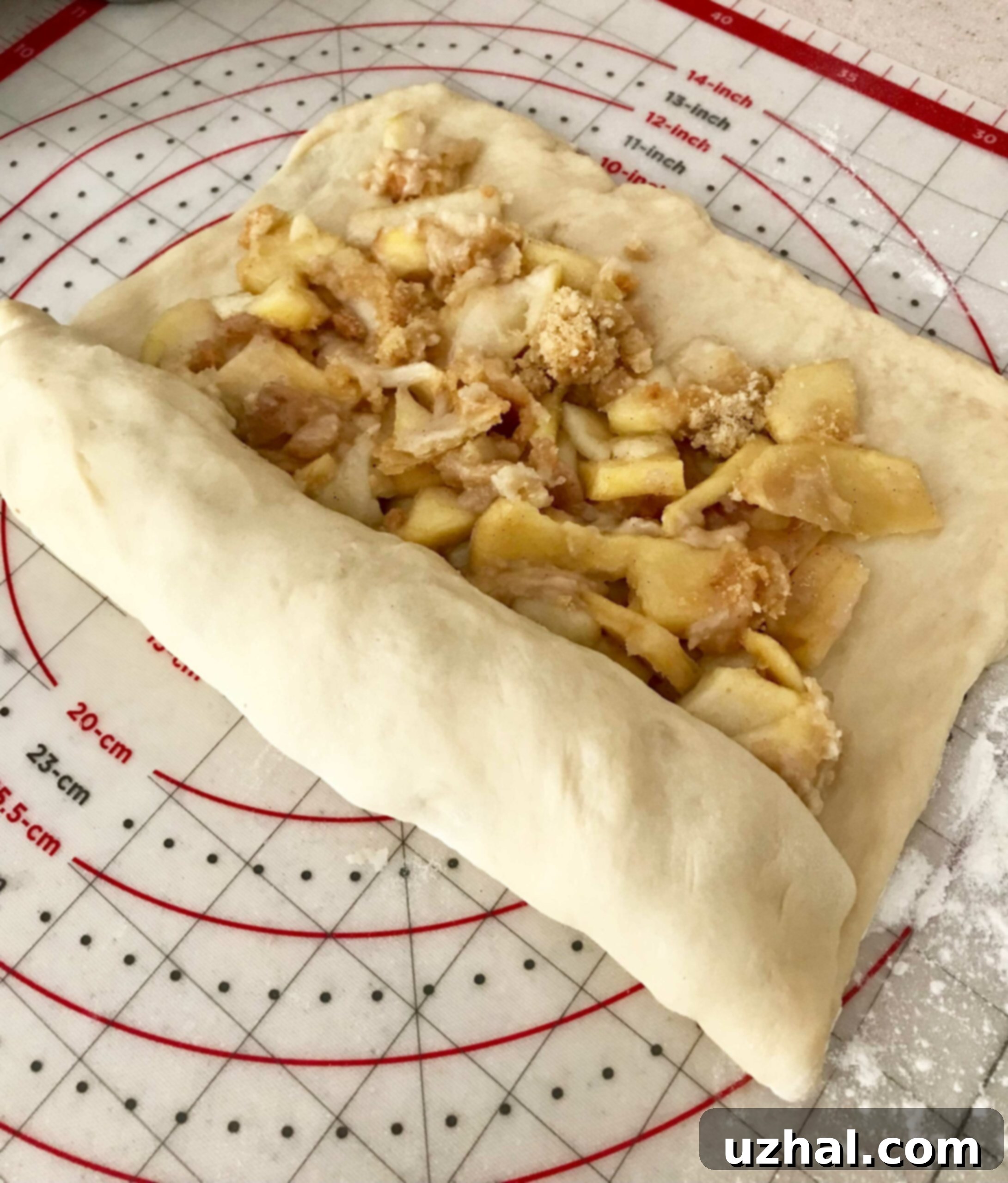 Cinnamon roll dough generously spread with chopped apple pie filling, in the process of being rolled up.