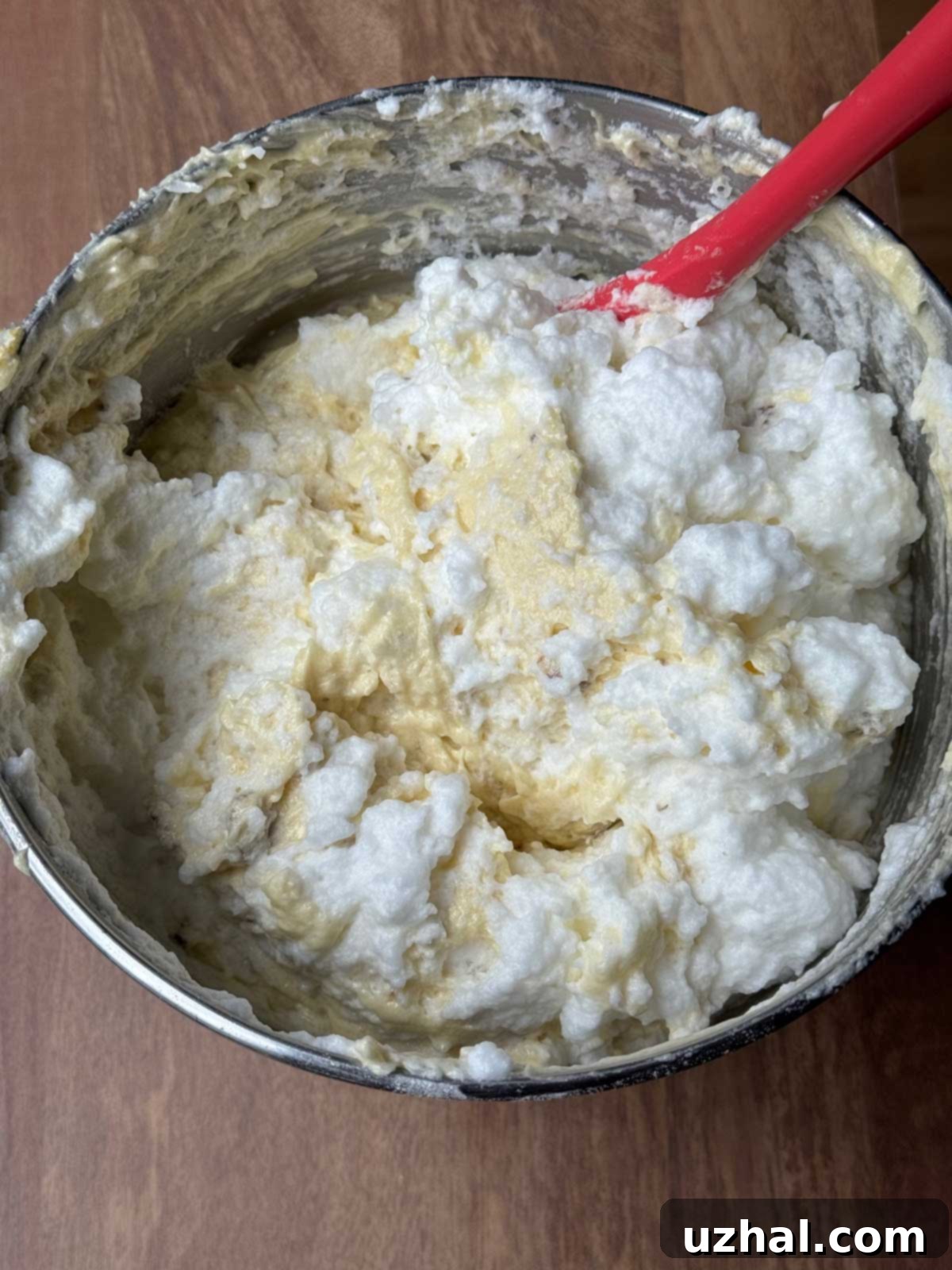 Fluffy egg whites being gently folded into Italian Cream Cake batter, ensuring a light and airy texture.