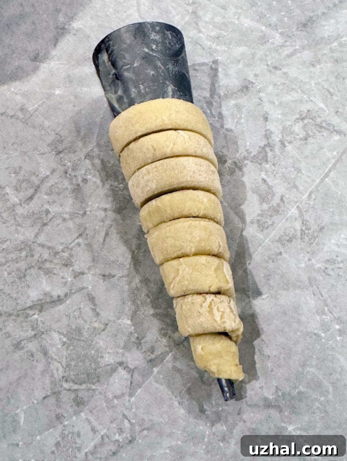 Puff pastry dough wrapped around a cream horn mold, ready for baking