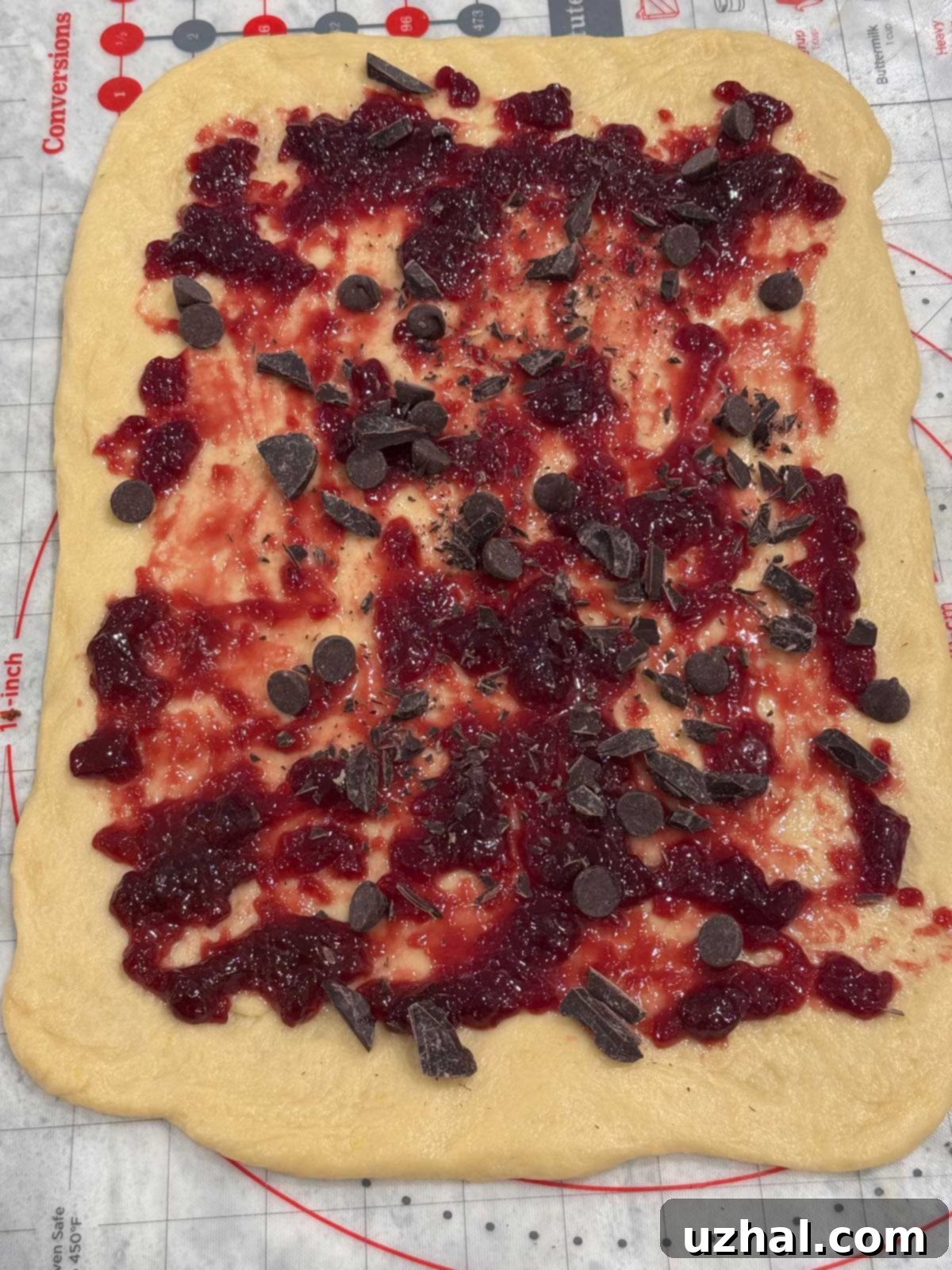 Babka dough spread flat on a pastry mat with a layer of fruit preserves and chocolate, ready for rolling.