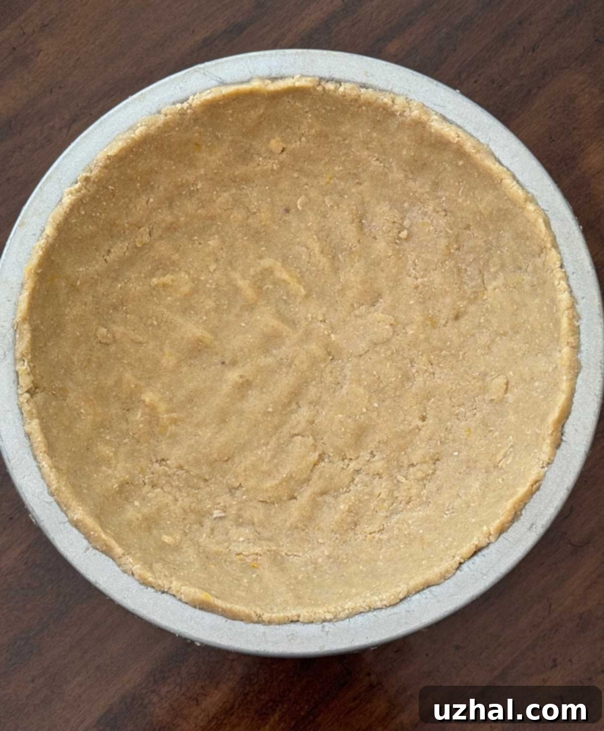 An unbaked Gluten-Free Crumb Crust, perfectly pressed into a pie dish, ready for its initial bake and then to hold the creamy ricotta sour cream filling.