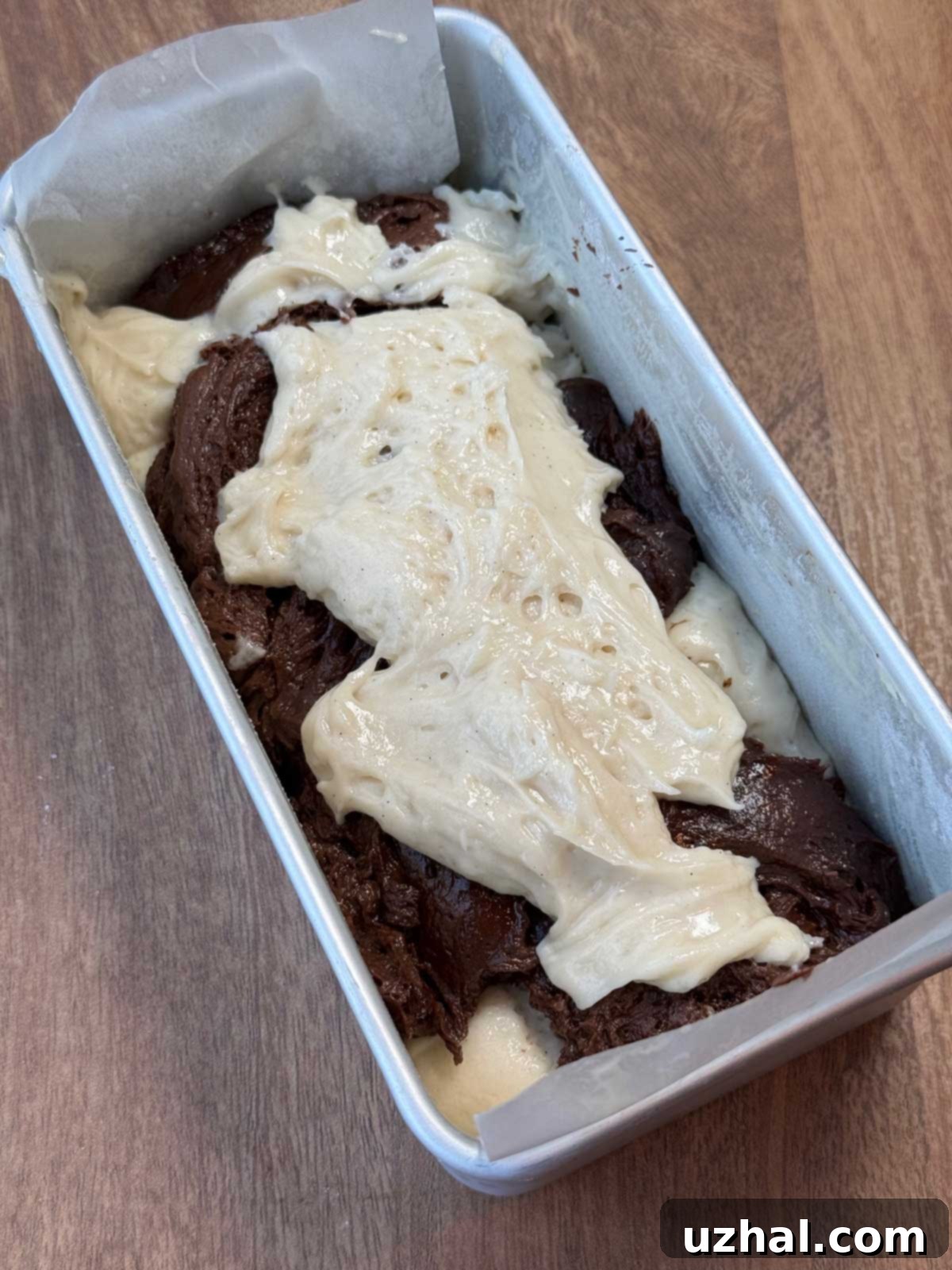Tofu marble cake batter being swirled in an 8x4 inch loaf pan, showing the vanilla and chocolate sections.