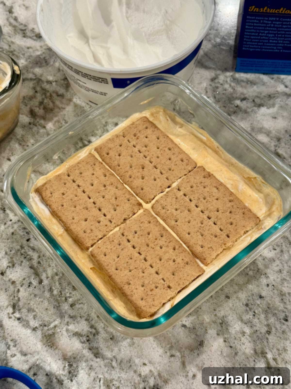 Layers of graham crackers and pumpkin filling being assembled in a pan for an eclair cake.