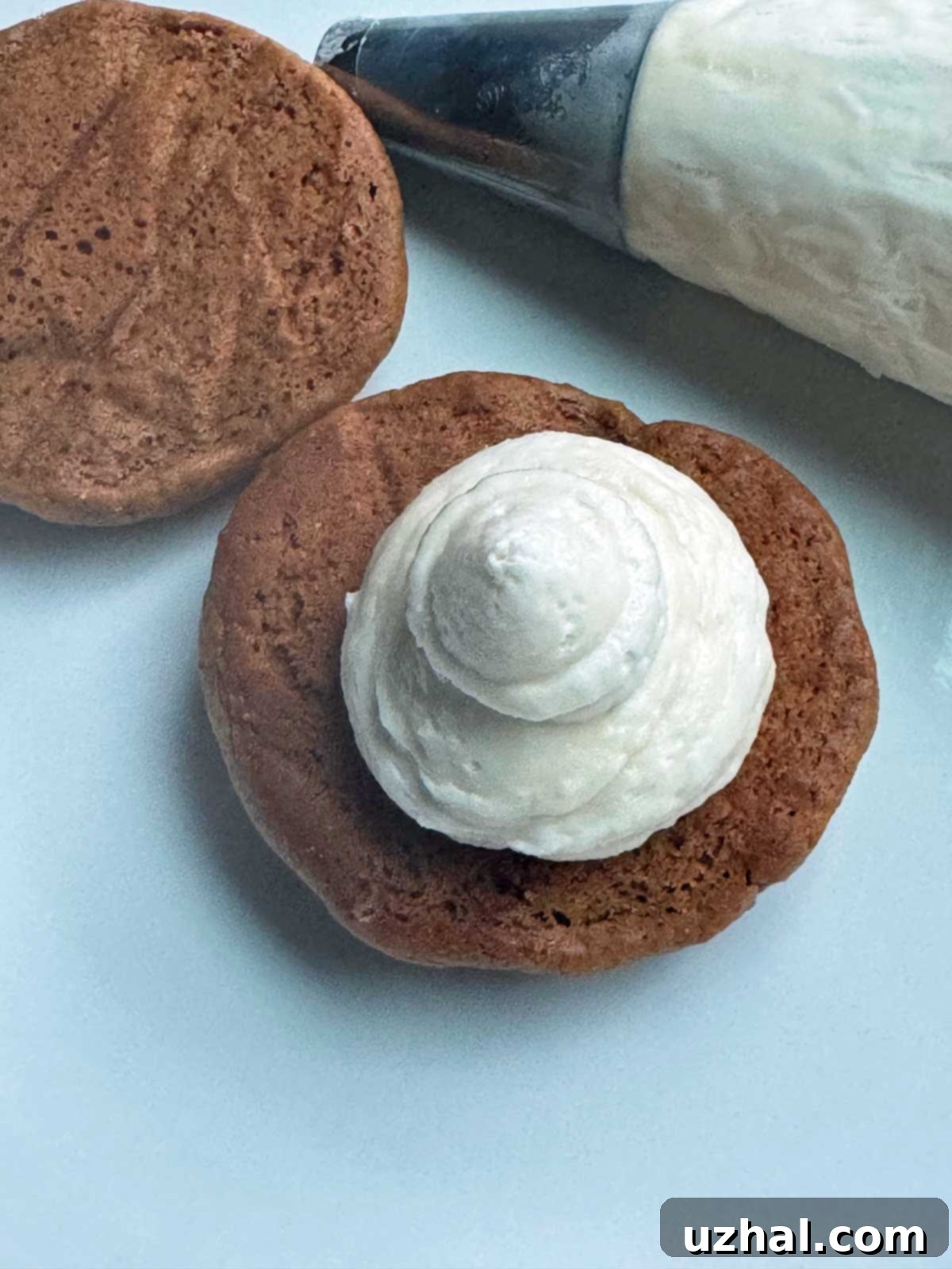 A gingerbread whoopie pie with filling piped out of a pastry bag.